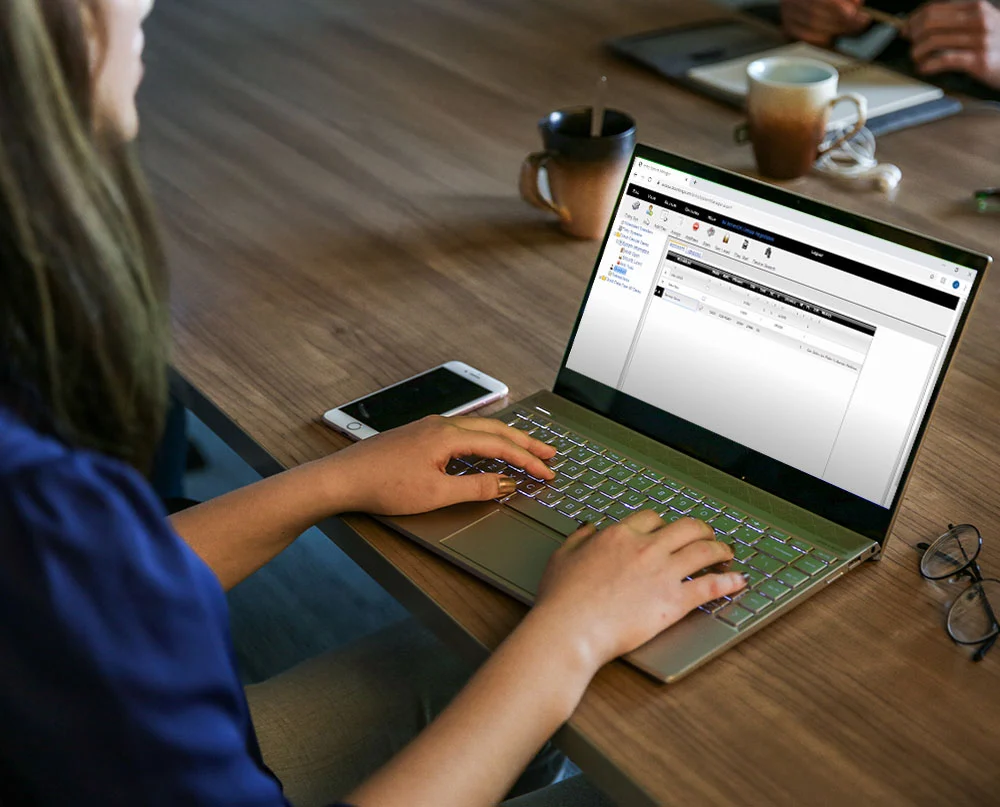 Person using a laptop with DKS Cloud Account Manager software on screen, seated at a table with a phone and coffee mugs nearby.
