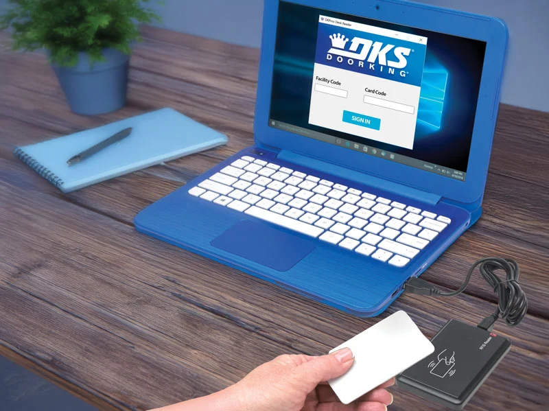 Person using a DKS USB card scanner connected to a blue laptop displaying the Doorking card reader software