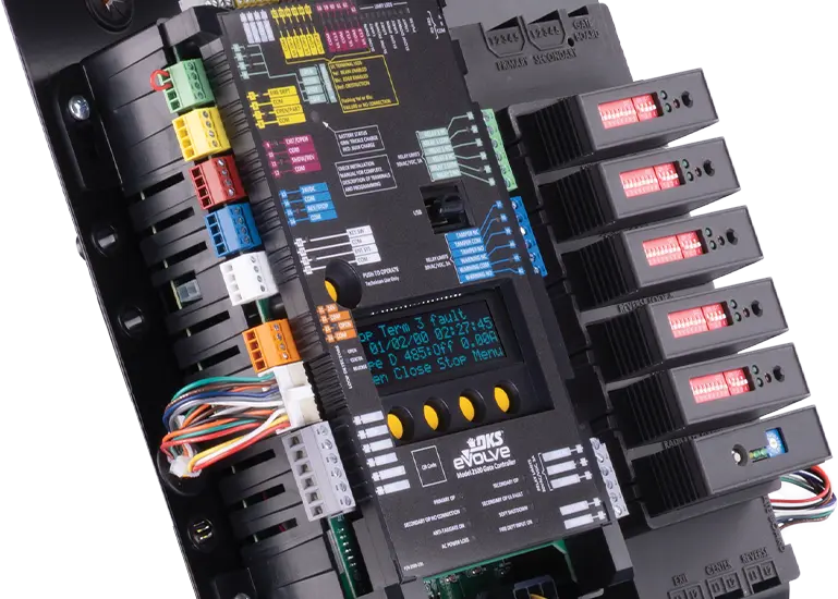 DoorKing 2170 eVolve controller board for slide gate operator, shown in a product close-up view. The rectangular green circuit board features numerous electronic components including capacitors, relays, terminal blocks, microchips, and connectors. A prominent blue LED display screen is visible in the center with onboard programming controls, part of DoorKing's eVolve series smart gate automation system.